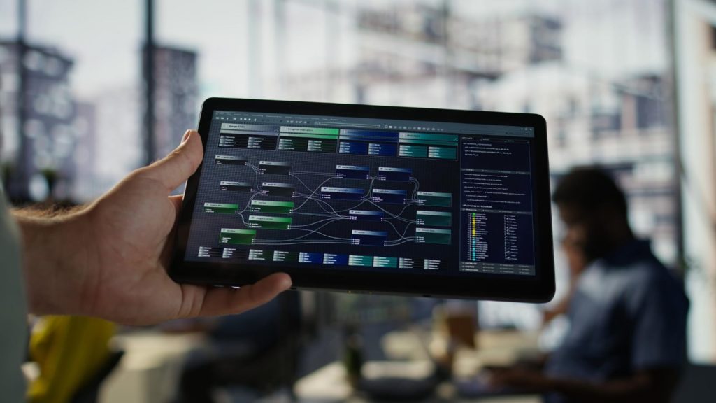 Hand holding a tablet displaying a complex system architecture or data flow diagram in an office setting.