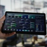 Hand holding a tablet displaying a complex system architecture or data flow diagram in an office setting.