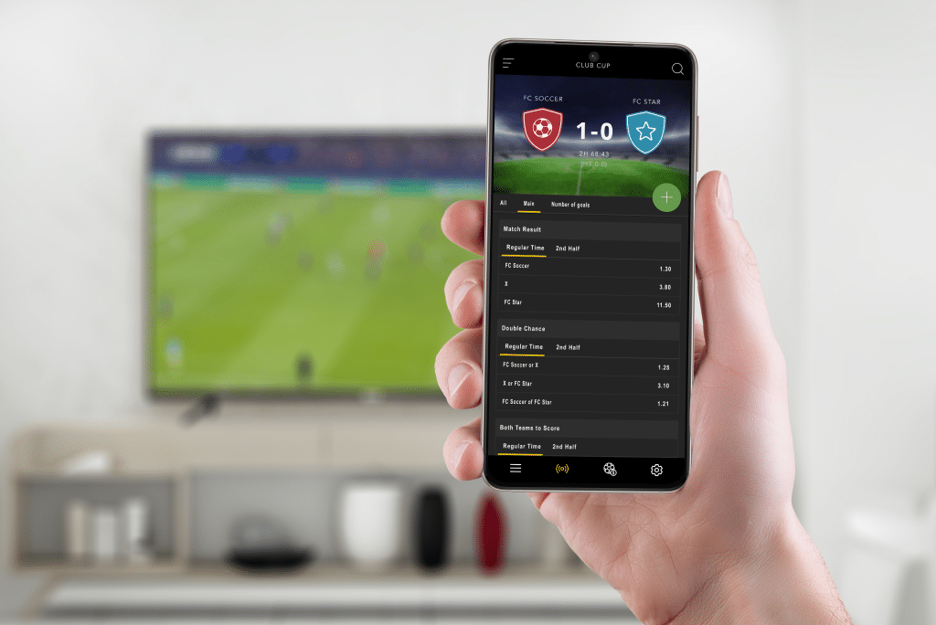 Person using a mobile sports betting app while watching a live football match – example of iGaming software development