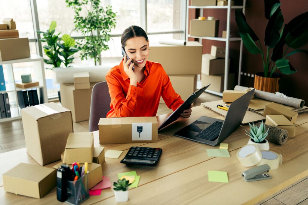 Woman managing e-commerce orders at her workplace using a laptop and phone in a professional office setup. Ecommerce solution implementation and optimisation