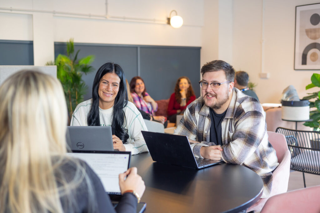 Spyrosoft employees in Bournemouth brainstorming. Next to a man wearing glasses sits a dark-haired woman, and opposite them sits a blonde woman.