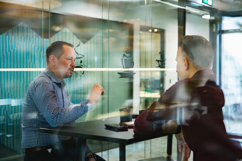 Two men are talking in the kitchen area of ​​Spyrosoft's Warsaw office. One is wearing a blue shirt, the other a solid burgundy one.