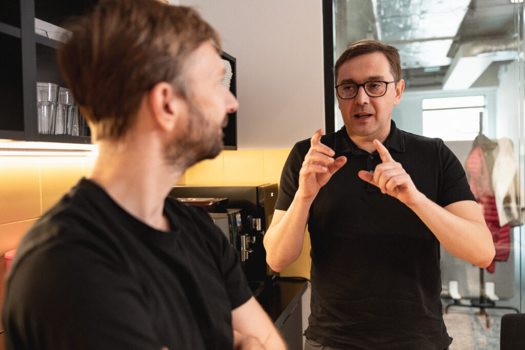 Two men, both Spyrosoft employees, talk to each other in the staff kitchen.