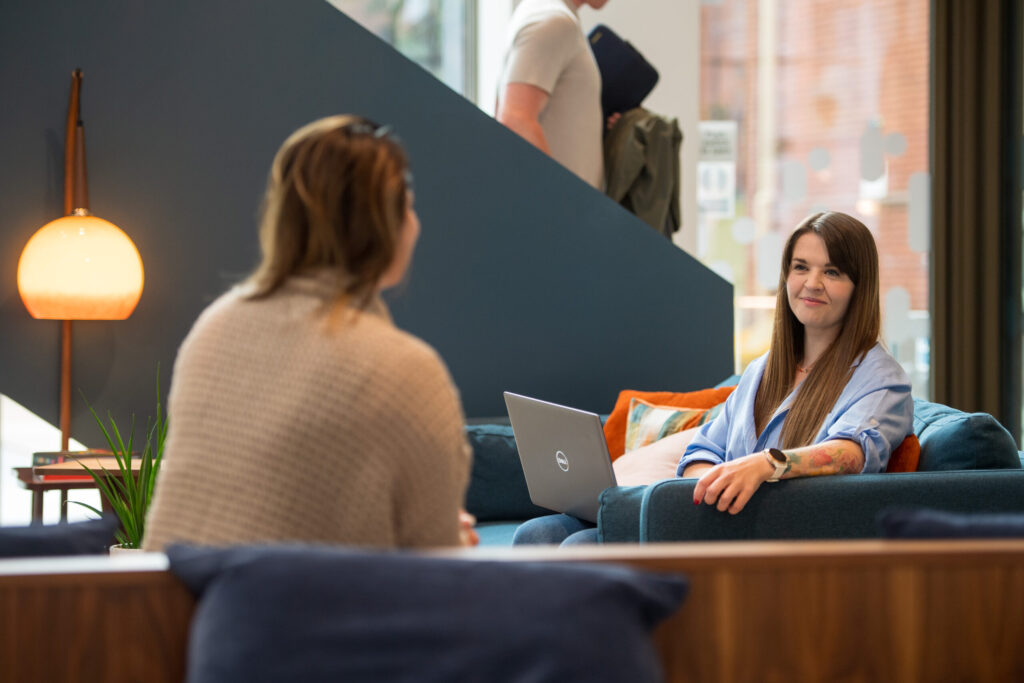 Two female employees of Spyrosoft in Manchester talk to each other in the common area of ​​the building