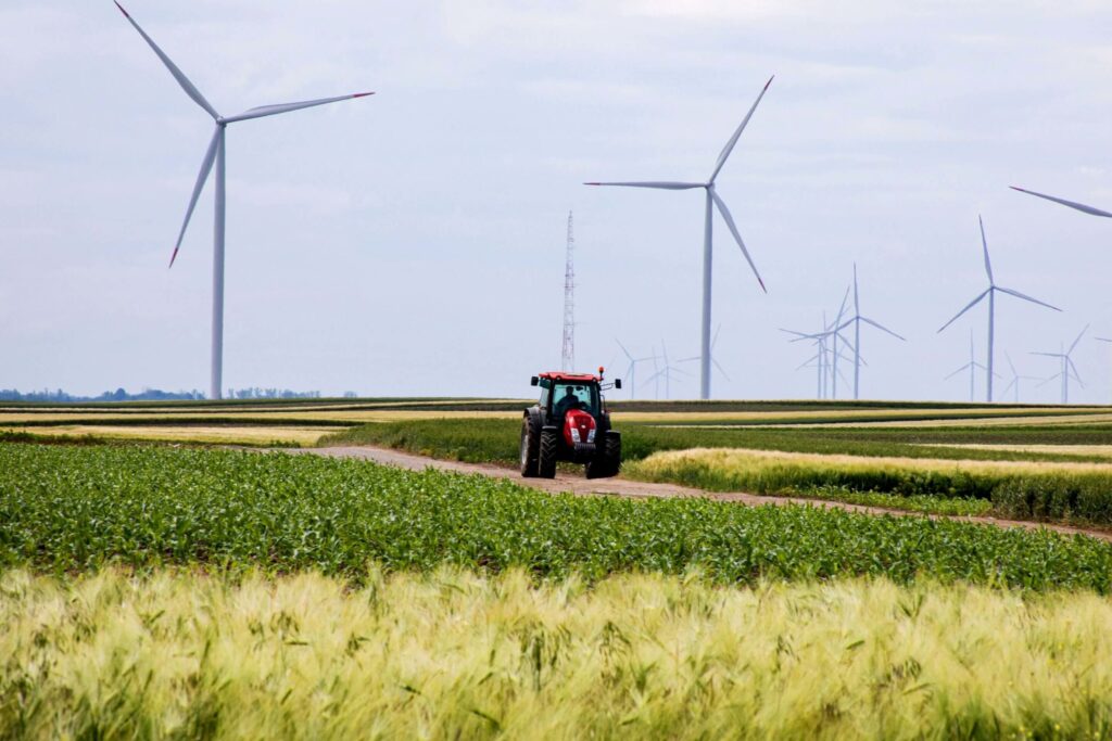 Tractor in lush green fields, sustainable agriculture operations amid towering wind turbines_Climate tech and sustainable agriculture 